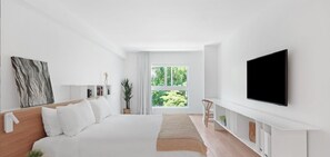 A modern bedroom with a large bed, a TV mounted on the wall, and a window with a view of greenery. - Beach Haus Bal Harbour (Bal Harbour)