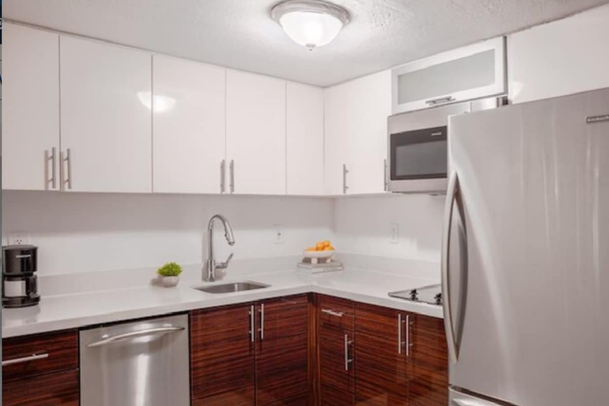 A modern kitchen with white cabinets, a stainless steel refrigerator, a microwave, and a dishwasher.
