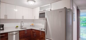 A modern kitchen with white cabinets, a stainless steel refrigerator, a microwave, and a dishwasher. - Beach Haus Bal Harbour (Bal Harbour)