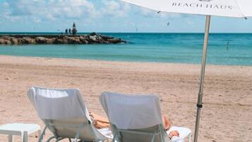 A beach scene with two beach chairs and a small table under a beach umbrella.