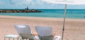 A beach scene with two beach chairs and a small table under a beach umbrella. - Beach Haus Bal Harbour (Bal Harbour)