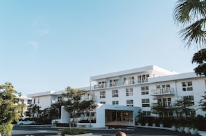 Um hotel moderno com fachada branca, várias varandas e um estacionamento.