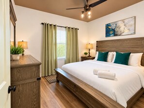 A hotel room with a bed, a nightstand, a ceiling fan, a window with curtains, and a painting on the wall. - Fun For Everyone!  Family Friendly Pool Home! (Thousand Palms)
