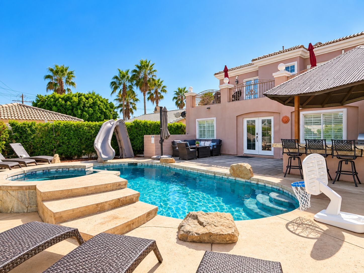 A swimming pool with a slide, lounge chairs, and a patio area with outdoor furniture.