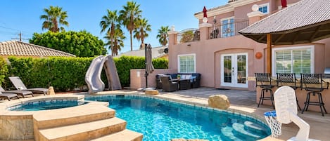 A swimming pool with a slide, lounge chairs, and a patio area with outdoor furniture.