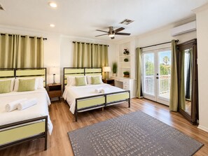 A hotel room with two beds, a desk, a chair, a ceiling fan, and a view of the outdoors.