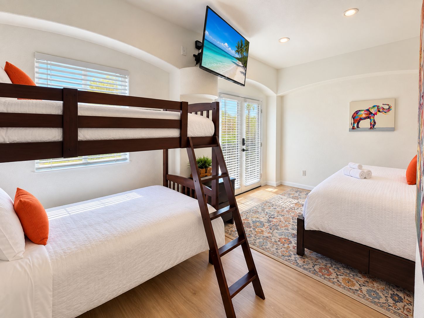 A hotel room with bunk beds, a television, a painting, and a door leading to a balcony.