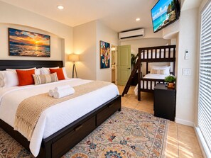 A hotel room with a large bed, a bunk bed, a TV, and a door leading to a bathroom. - Fun For Everyone!  Family Friendly Pool Home! (Thousand Palms)