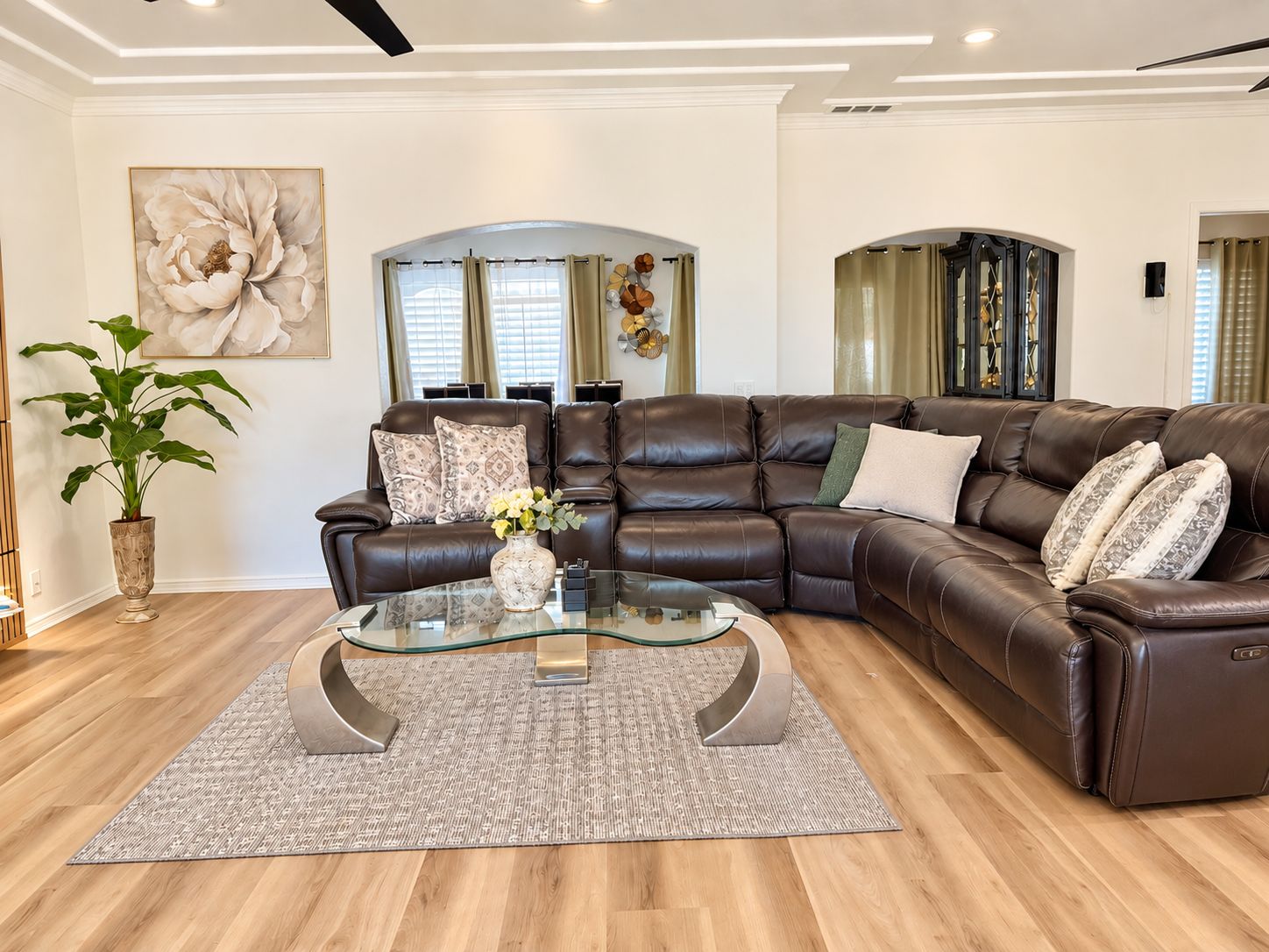 A modern living room with a leather sectional sofa, a glass coffee table, and a large floral painting on the wall.