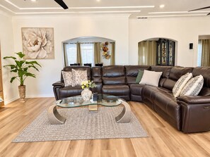 A modern living room with a leather sectional sofa, a glass coffee table, and a large floral painting on the wall.