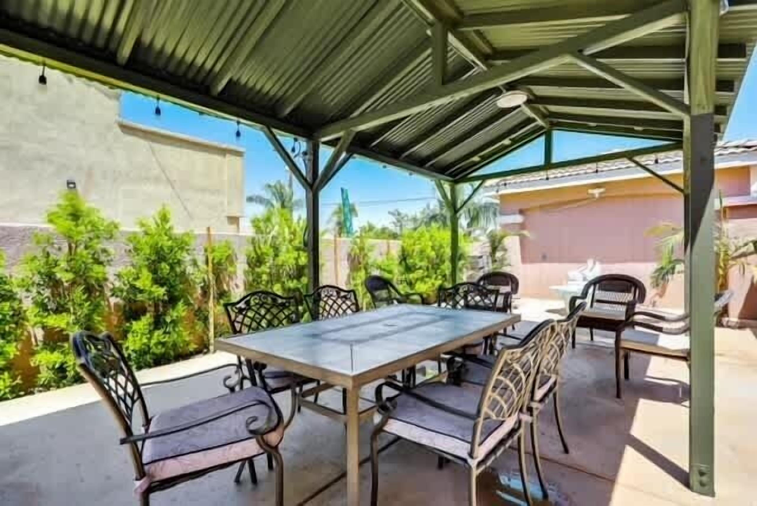 Een overdekte terras met een tafel en stoelen, omringd door groen.