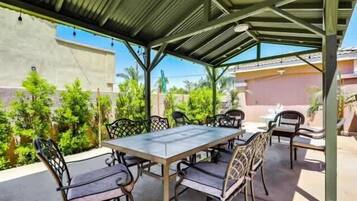 Een overdekte terras met een tafel en stoelen, omringd door groen.