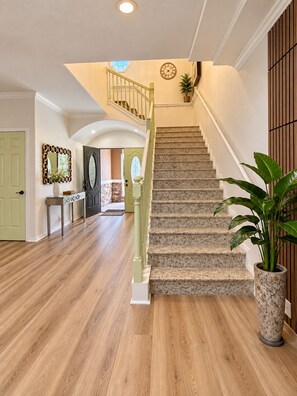 A staircase with a handrail, a potted plant, and a wall clock.