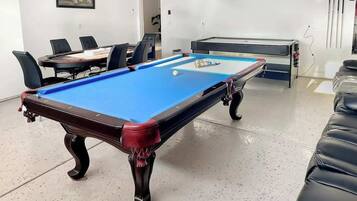 Een pooltafel met een blauwe viltkleed, omringd door zwarte lederen stoelen.