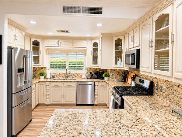 A modern kitchen with granite countertops, stainless steel appliances, and light-colored cabinetry. - Fun For Everyone!  Family Friendly Pool Home! (Thousand Palms)