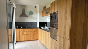 A modern kitchen with wooden cabinets, a stainless steel oven, and a black countertop. - Spacious, bright apartment close to the bay's beaches (Quiberon)