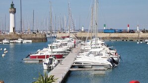 A marina with multiple boats docked along a wooden pier, a lighthouse in the background, and a clear sky. - Spacious, bright apartment close to the bay's beaches (Quiberon)