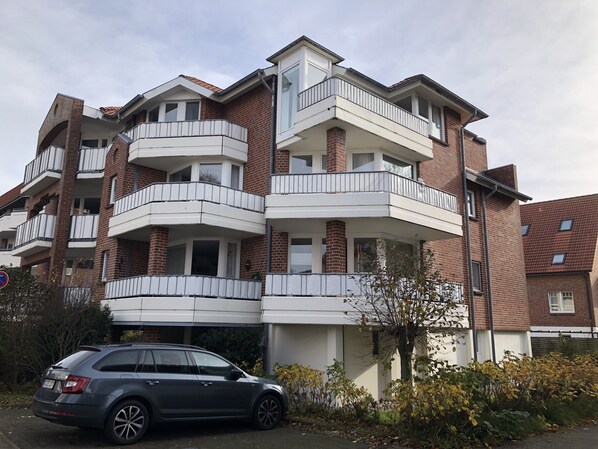 Un edificio residencial de varios pisos con balcones, un área de estacionamiento y un automóvil estacionado al frente.