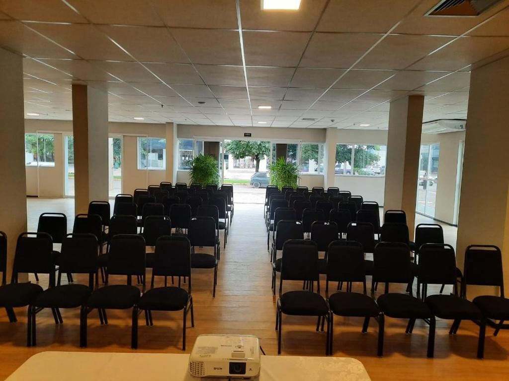 Ein Konferenzraum mit Reihen von Stühlen, einem Projektor und großen Fenstern.
