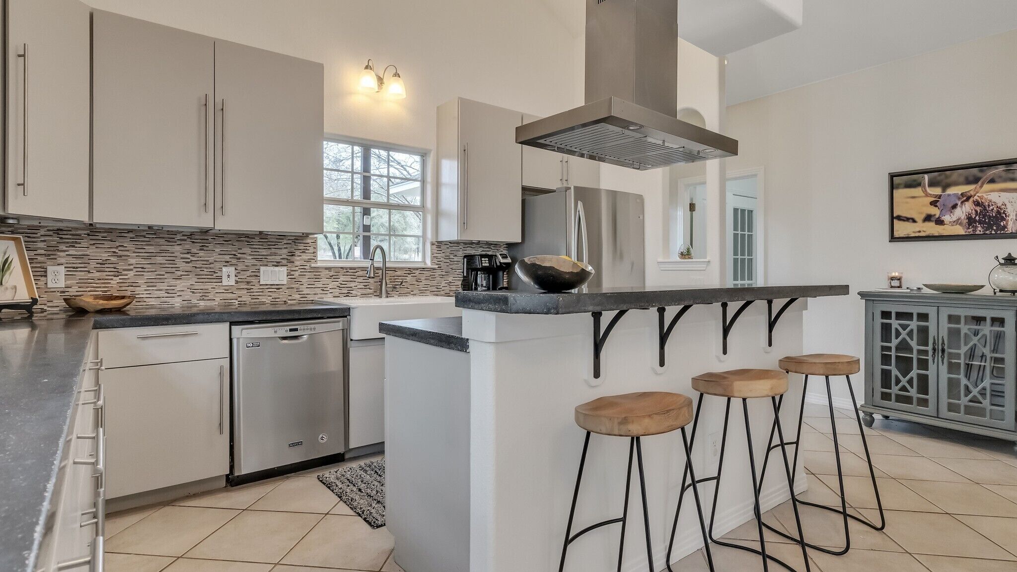 A modern kitchen with a dishwasher, a large island with stools, and a decorative backsplash.