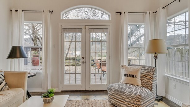 Ein gemütliches Wohnzimmer mit einem großen Bogenfenster, einer Couch mit gemusterten Kissen, einem Couchtisch mit einer Pflanze und einer Lampe.