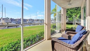 Un balcon doté de meubles en osier, de grandes fenêtres et offrant une vue sur un port de plaisance.