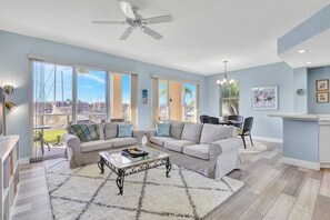 A spacious living room with a large window, a ceiling fan, and a dining area with a bar.