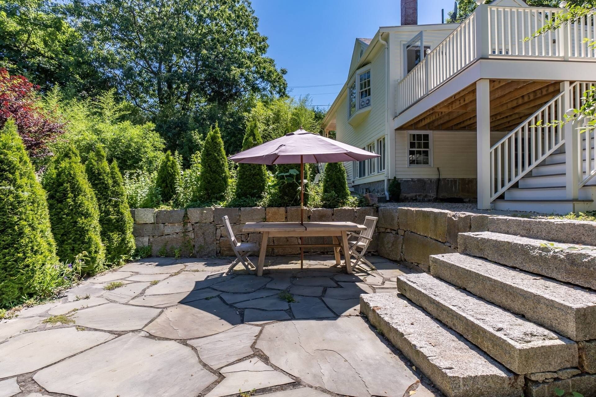 A patio with stone flooring, a wooden table, and a purple umbrella.