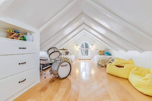 A spacious attic room with a high ceiling, wooden flooring, a drum set, a piano, and a cozy seating area with a yellow bean bag. - Sea Star (Rockport)