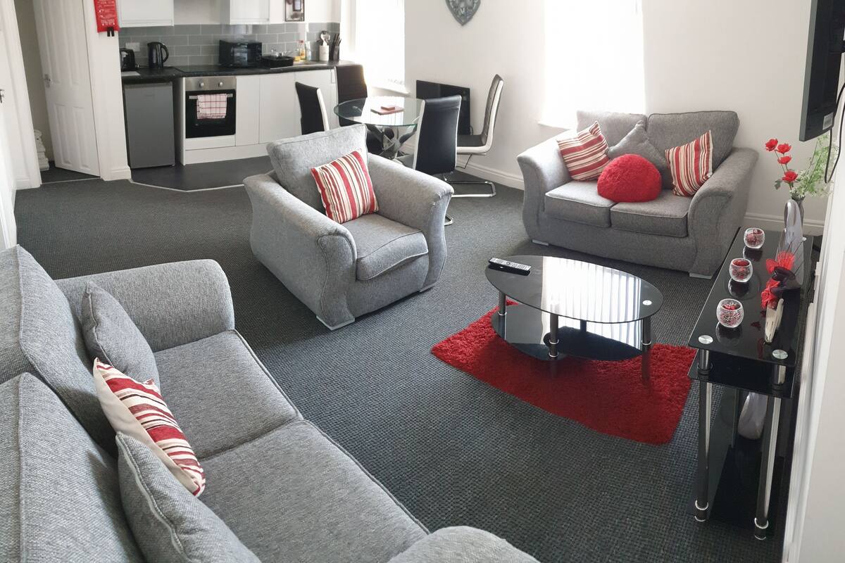 Un salon moderne avec des canapés gris, une table basse en verre et un tapis rouge.