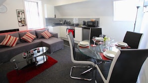Uma sala de estar moderna com um sofá cinza, uma mesa de centro de vidro e um espaço de jantar com mesa e cadeiras de vidro.