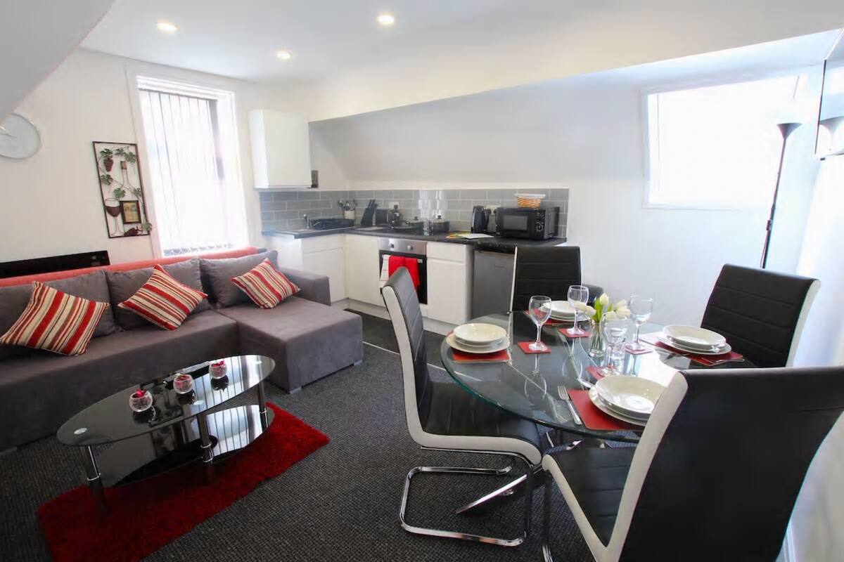 Ein modernes Wohnzimmer mit grauem Sofa, einem Glastisch und einem Essbereich mit Tisch und Stühlen.