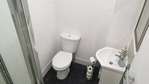 A small, clean bathroom with a toilet, sink, and a glass shower enclosure. - Coast Accommodation Station Road Apartments (Blackpool)