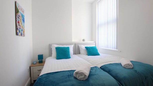 Quarto de hotel com duas camas, paredes brancas, janela com persianas e um quadro na parede.