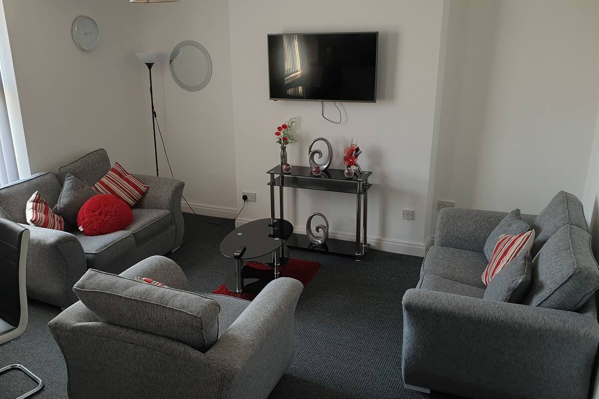 Ein modernes Wohnzimmer mit grauen Sofas, einem schwarzen Couchtisch und einem an der Wand befestigten Flachbildfernseher.