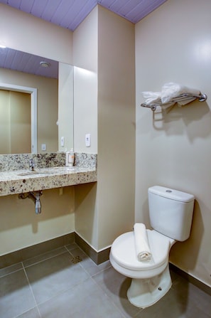 A bathroom with a white toilet, a sink with a marble countertop, and a mirror above the sink. - Fit Transamerica Rondonópolis (Rondonopolis)