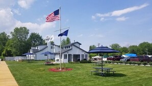 A grassy area with a flagpole, picnic tables, and a building with a porch.