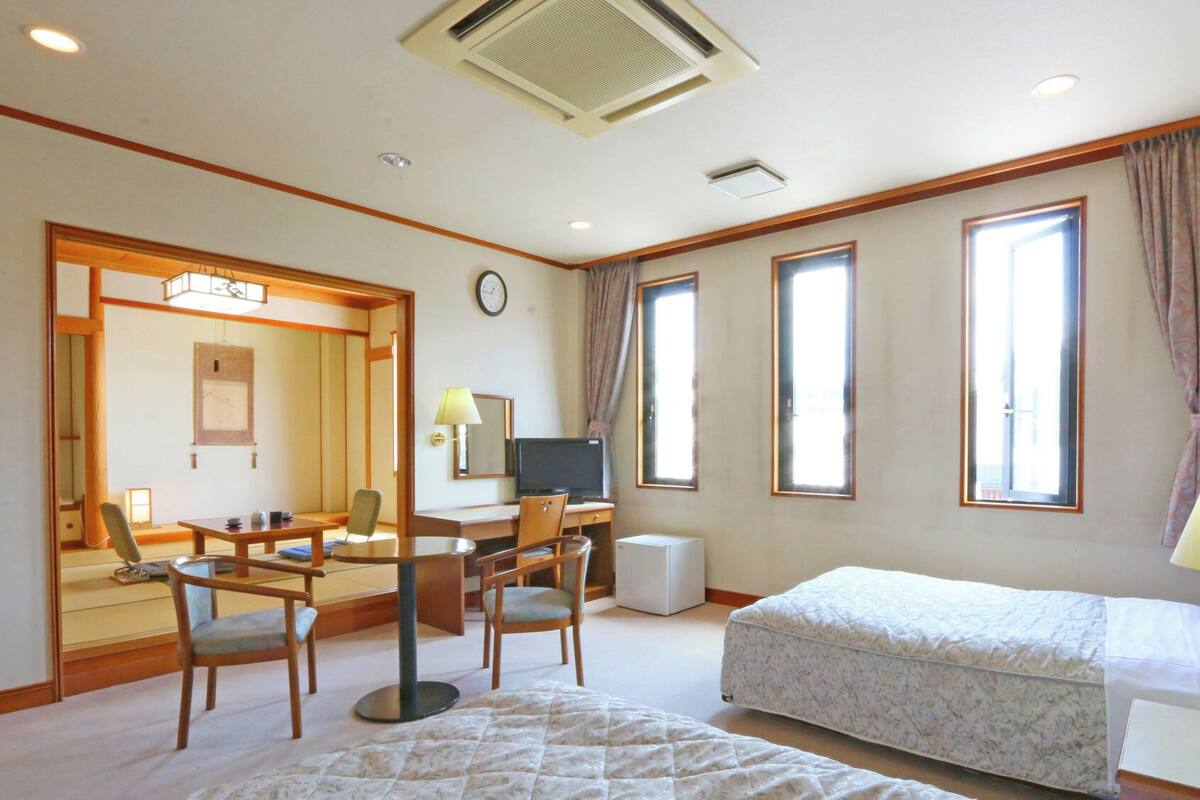 Habitación de hotel con cama, escritorio, silla, ordenador y un gran ventanal.