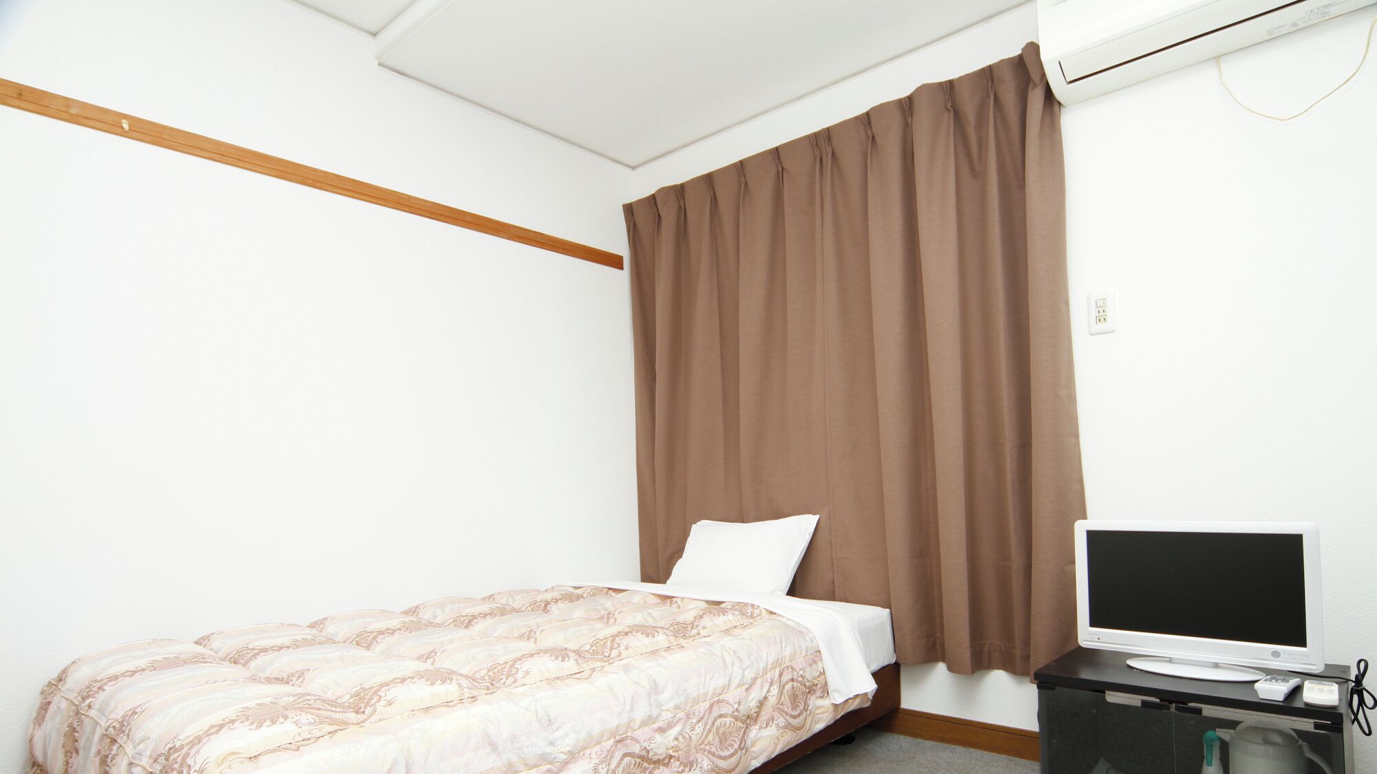 A hotel room with a bed, a television, and a window with brown curtains.