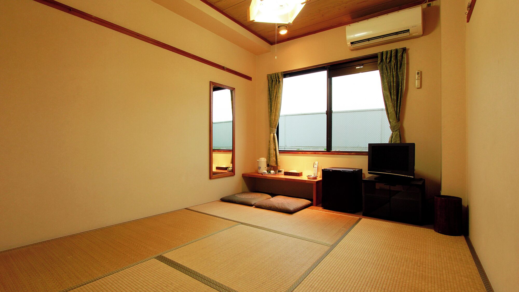 A room with tatami mats, a television, a small table with a lamp, and a window with curtains.