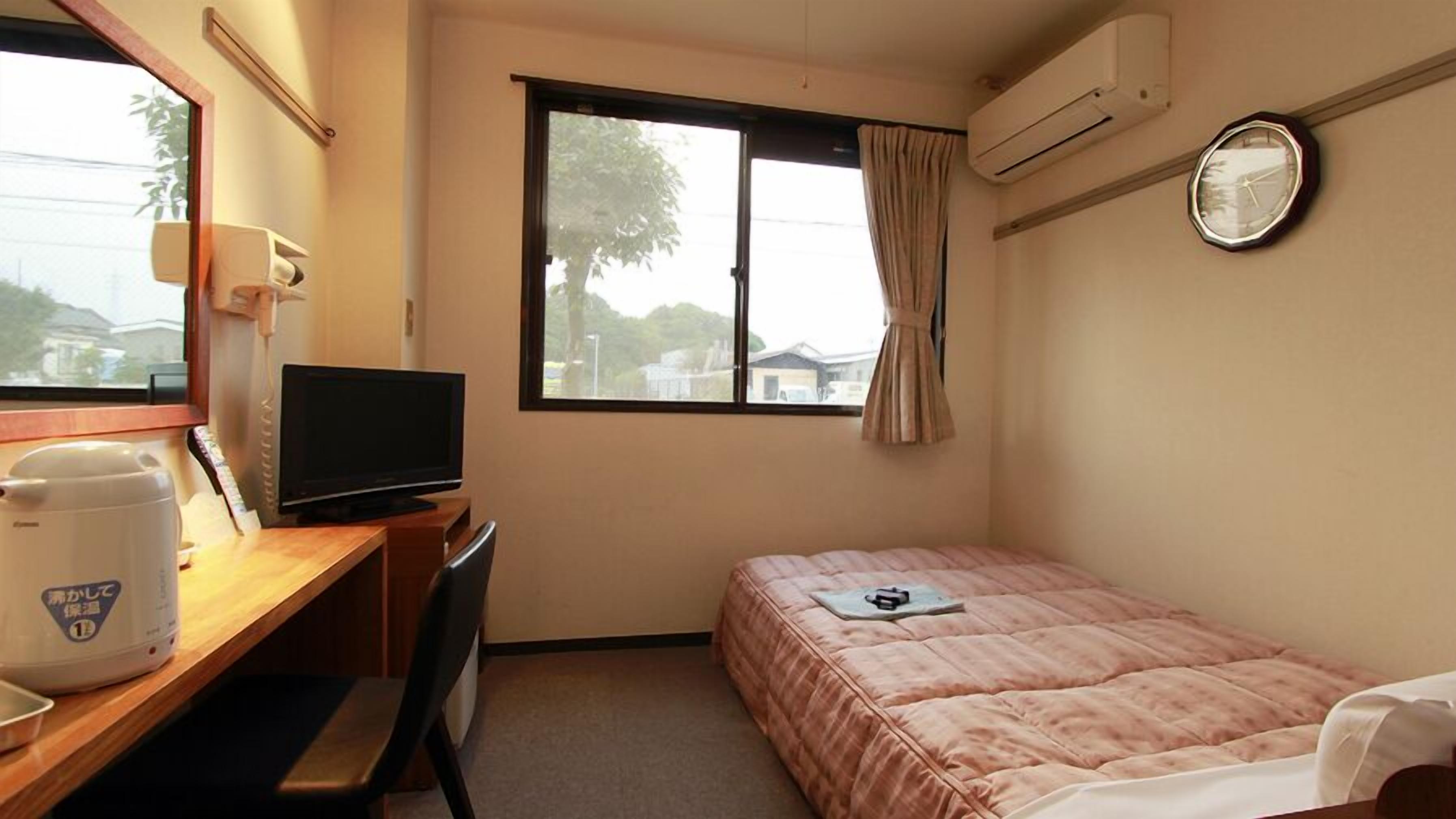 Une chambre d’hôtel comprenant un lit, un bureau avec une télévision, une fenêtre avec des rideaux et un appareil de climatisation.