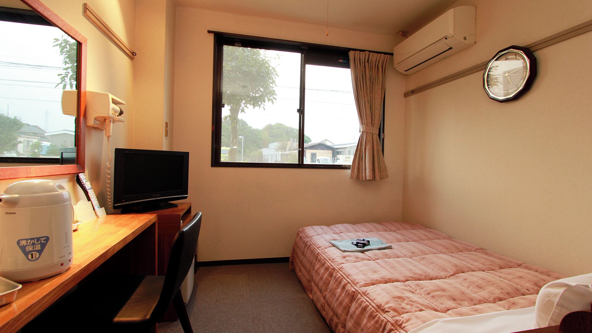 A hotel room with a bed, a desk with a TV, a coffee maker, a window with curtains, and an air conditioner.