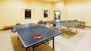 Una sala con cuatro mesas de ping pong, un banco y una puerta que da a otra habitación.