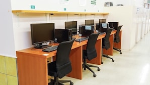 A row of computer workstations with chairs, each labeled with a number. - Niko Niko Capsule Hotel (Fukuchiyama)