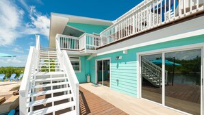 A two-story house with a wooden deck, a staircase, and a large sliding glass door. - Private Paradise, Waterfront Home - 15 minutes from Key West (Key West)