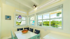 A bright dining area with a white table, teal chairs, and a bowl of fruit. Large windows offer views of greenery and a water body. - Private Paradise, Waterfront Home - 15 minutes from Key West (Key West)