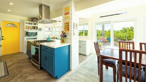 A bright kitchen with blue cabinets, a yellow door, and a dining area with wooden chairs. - Private Paradise, Waterfront Home - 15 minutes from Key West (Key West)