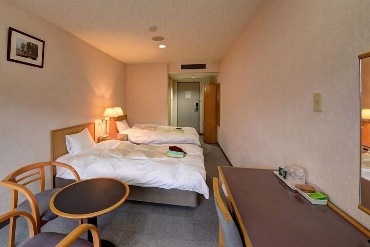 Une chambre d’hôtel avec deux lits, une petite table, une chaise et une lampe de chevet.