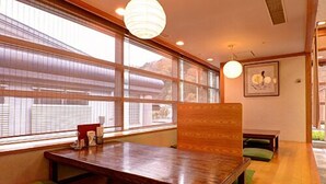 Una habitación con una mesa de madera, asientos acolchados verdes, ventanas amplias y una lámpara colgante.