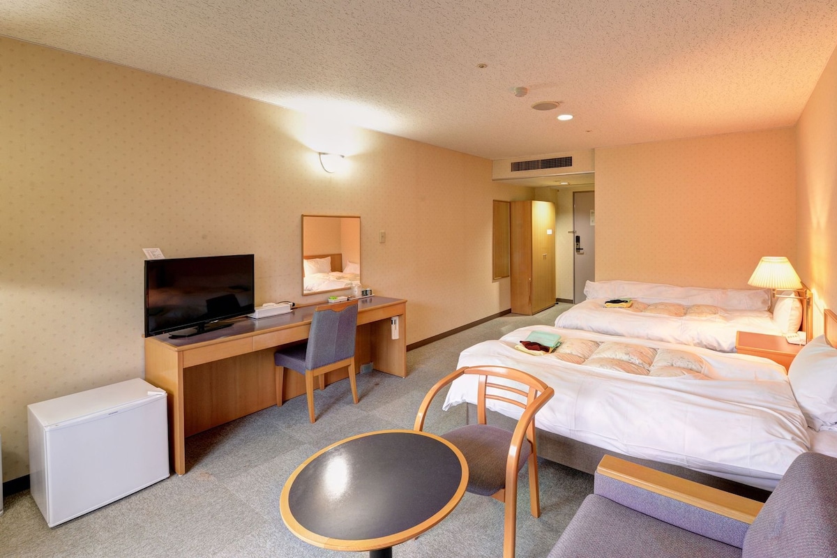 Ein Hotelzimmer mit einem Bett, einem Schreibtisch mit Fernseher, einem Sessel, einem kleinen Tisch und einem Kleiderschrank.
